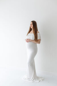 mom in white dress holding her pregnant belly